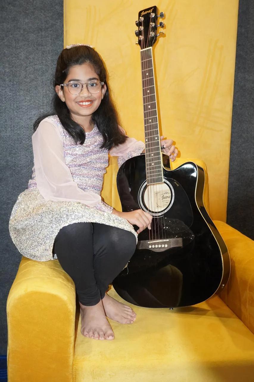 Young student posing with an acoustic guitar in the studio